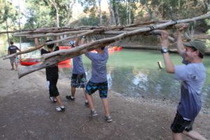 ילדים במחנה קיץ סוחבים סנדות ליד הקיאקים