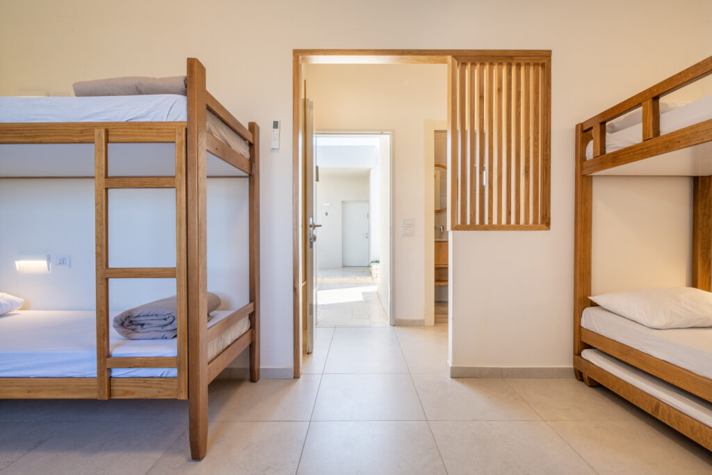 פנים חדר בבית ספר שדה אכזיב. מיטות קומותיים ומבט לכיוון הכניסה לחדר למסדרון בחוץ 