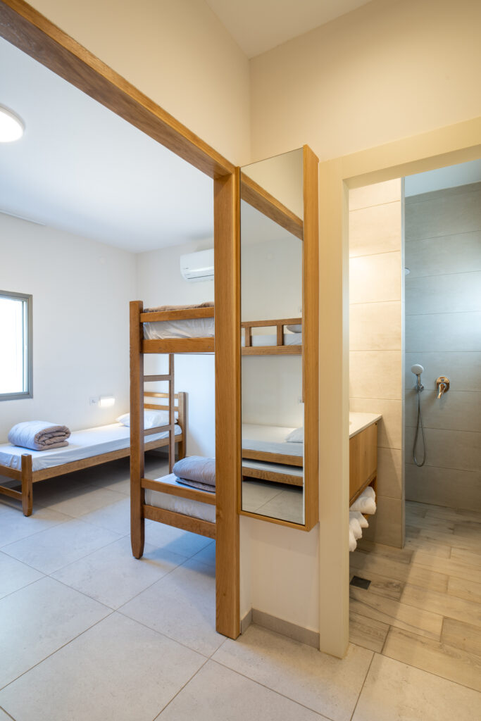 פנים חדר בבית ספר שדה אכזיב. מיטות קומותיים מראה ומבט הצצה לתוך חדר המקלחת 