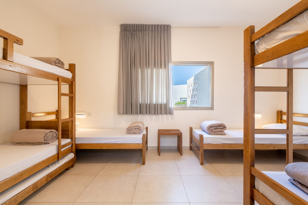 פנים חדר בבית ספר שדה אכזיב. מיטות קומותיים וחלון עם וילון אפור 