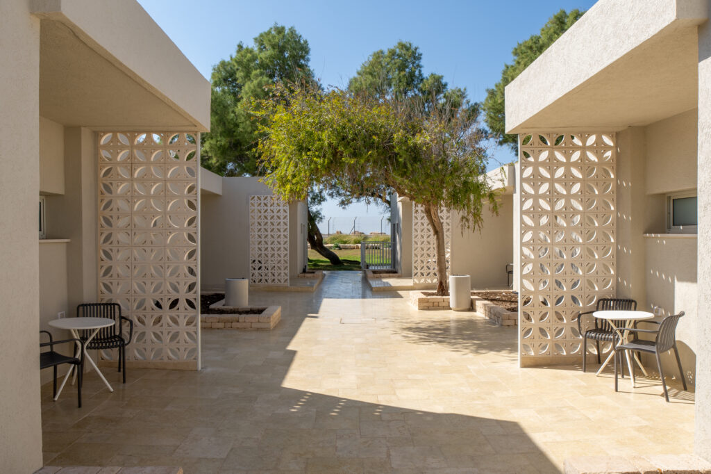 מבאות חדרים בשביל גישה לחדרים בבית ספר שדה אכזיב. אבנים לנות מבנים עץ וחתול בכניסה לאחד החדרים. נוף לים 