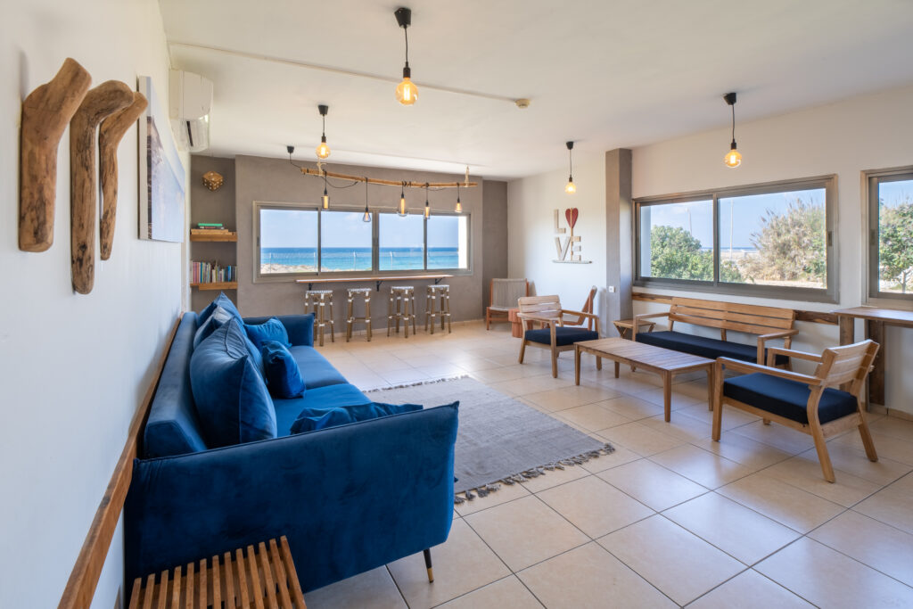 חדר המועדון בבית ספר שדה אכזיב, נוף לים, כורסאות ישיבה, ספה כחולה, שטחי וספרים 