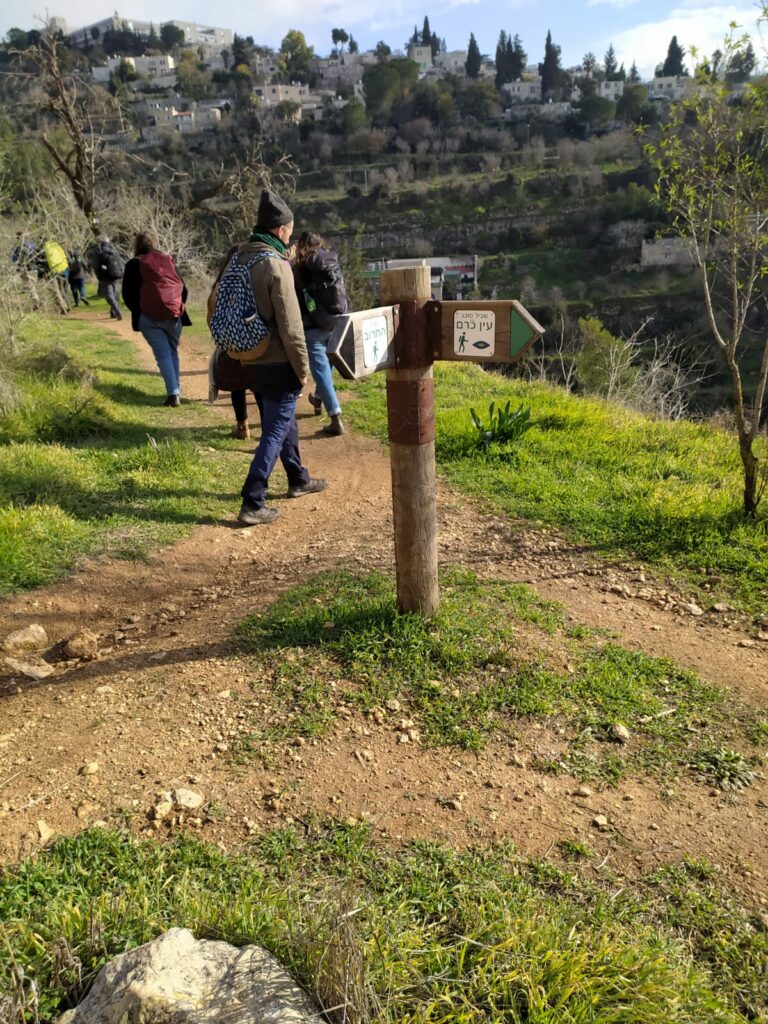 אנשים מטיילים בשביל ירוק בחורף, לצד גבעה עם בתים 