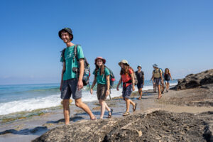 מטיילים הולכים בחוף אכזיב עם תיקים וכובעים מבט מקדימה