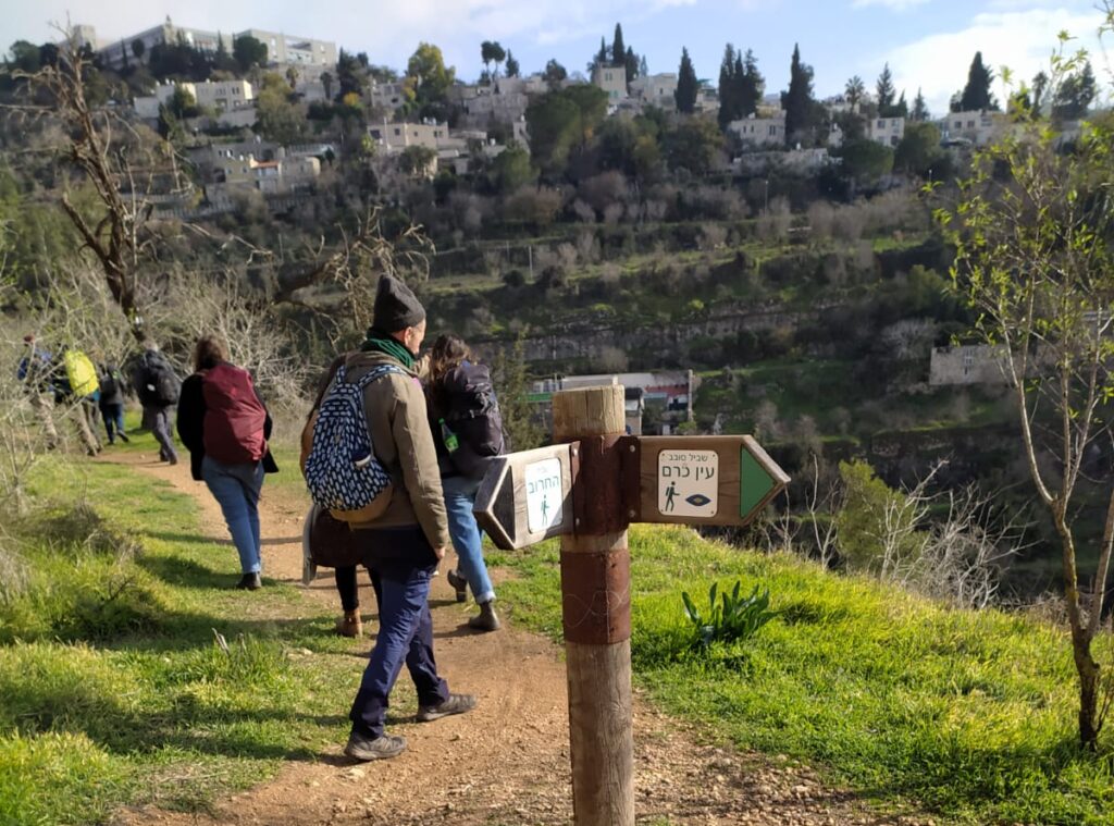 אנשים מטיילים בשביל ירוק בחורף, לצד גבעה עם בתים