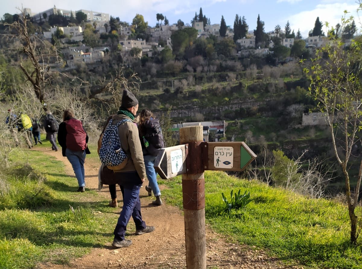 אנשים מטיילים בשביל ירוק בחורף, לצד גבעה עם בתים