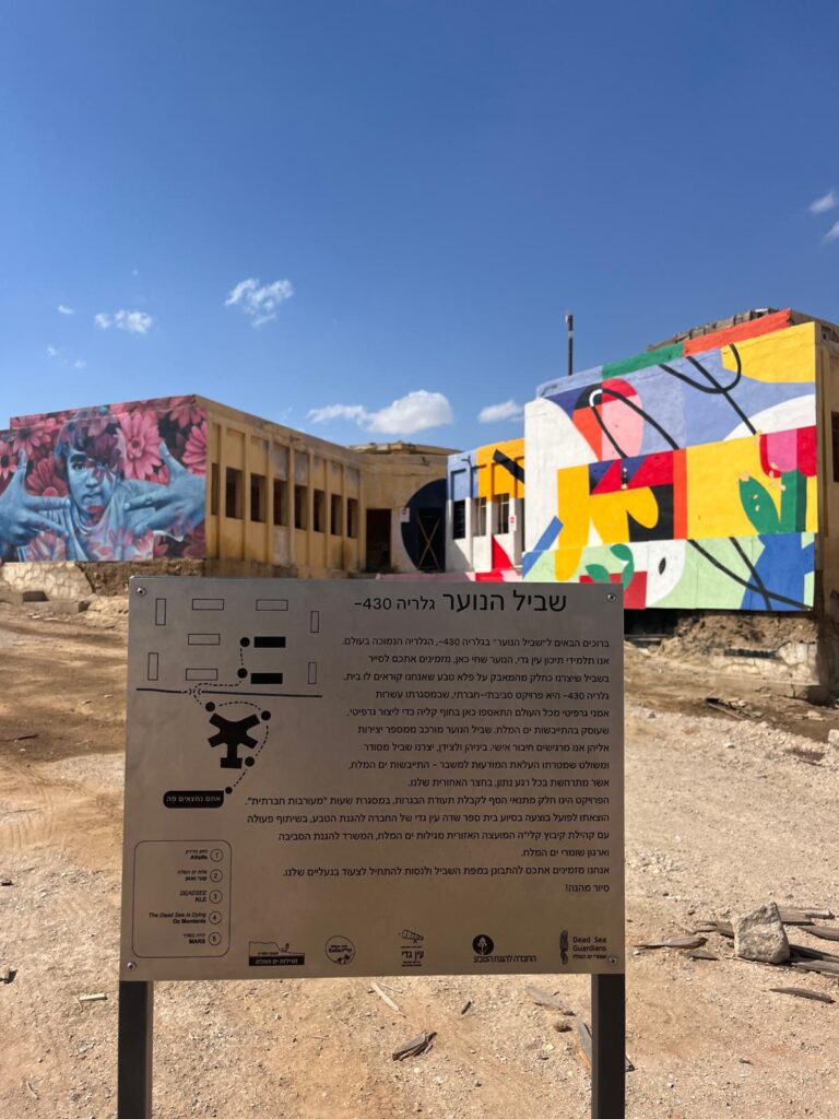 שלט של גלריה 430 המספר על שביל הנוער וברקע מבני גרפיטי 