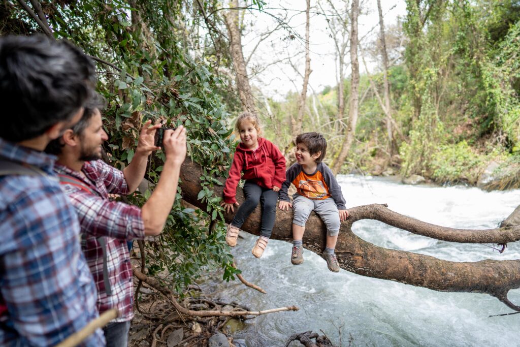 2 ילדים על ענף עץ גדול מעל נחל הבניאס מצטלמים לאבא שלהם שמצלם